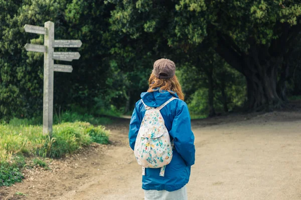 Woman looking at signpost in forest — Stock Photo, Image