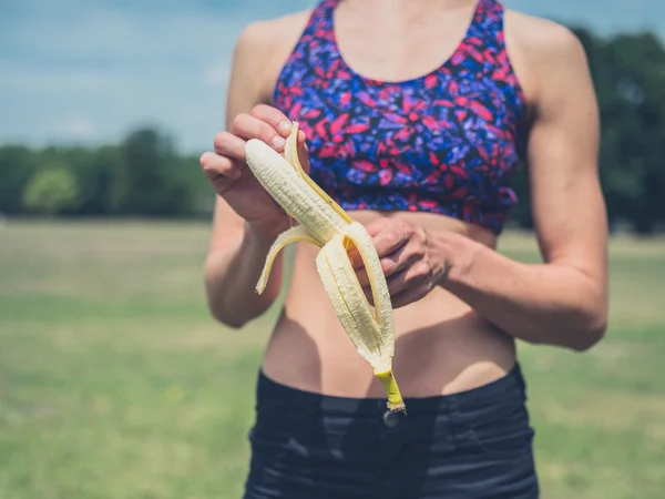 Dopasowanie kobieta peelingu bananów w parku — Zdjęcie stockowe