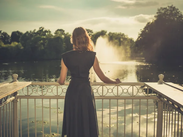 Young woman standing by lake at sunset — Stock Photo, Image