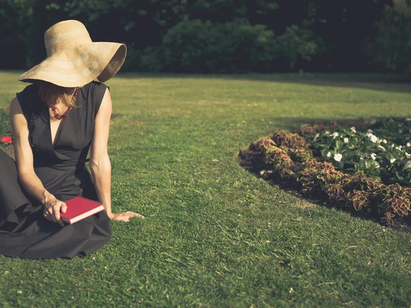 Elegant kvinna med hatt läsning i park — Stockfoto