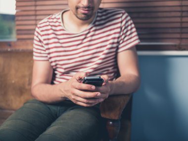 Genç adam evde akıllı telefon kullanıyor.