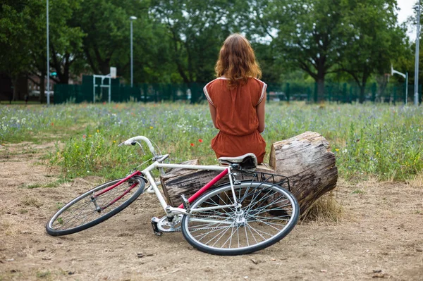Femme assise sur une bûche avec son vélo — Photo
