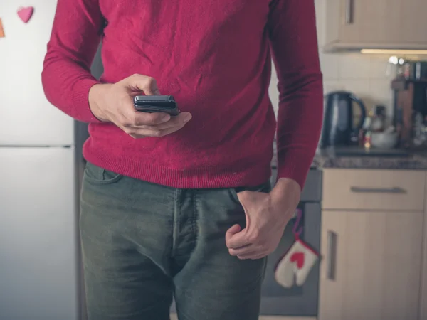 Junger Mann benutzt Smartphone in Küche — Stockfoto