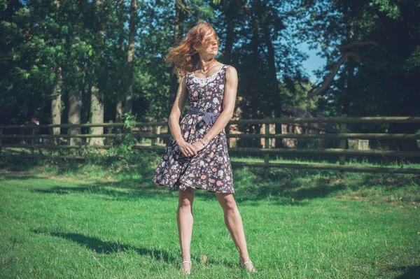 Junge Frau steht an Sommertag in Feld neben Zaun — Stockfoto