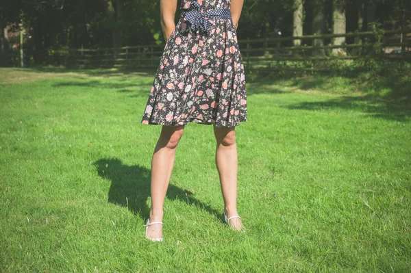 Young woman standing in field by fence on summer day — Stock Photo, Image