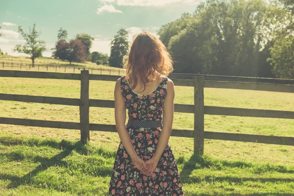 Jovem mulher em pé no campo por cerca no dia de verão — Fotografia de Stock