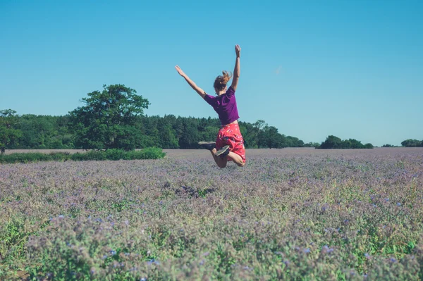 Szczęśliwa młoda kobieta skoki w dziedzinie fioletowe kwiaty — Zdjęcie stockowe
