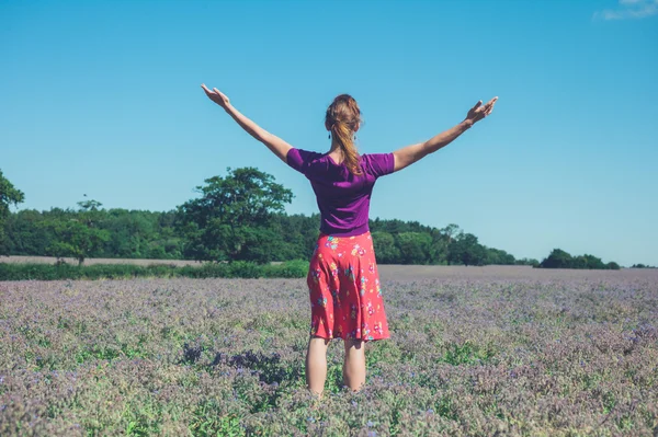 Mulher levantando os braços em um campo de flores roxas — Fotografia de Stock