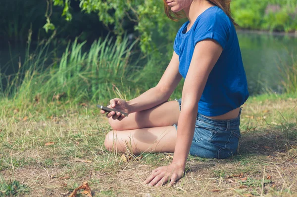 Mujer joven usando el teléfono inteligente por el agua en el parque —  Fotos de Stock