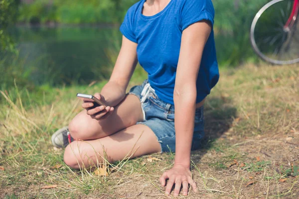 Mujer joven usando el teléfono inteligente por el agua en el parque — Foto de Stock