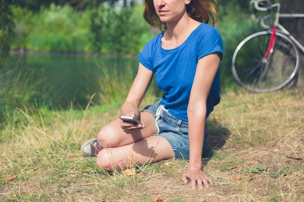 Jeune femme utilisant un téléphone intelligent par l'eau dans le parc — Photo