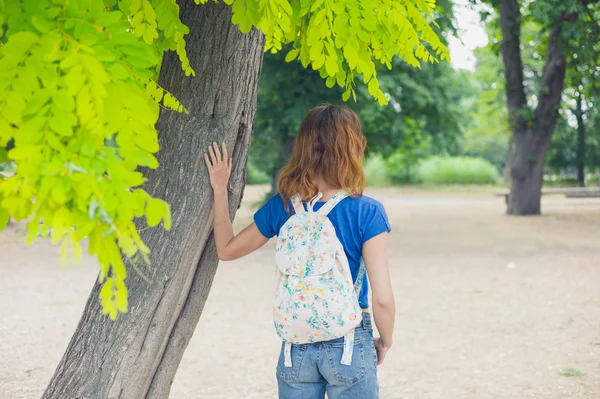 Молодая женщина, стоящая в парке на дереве — стоковое фото