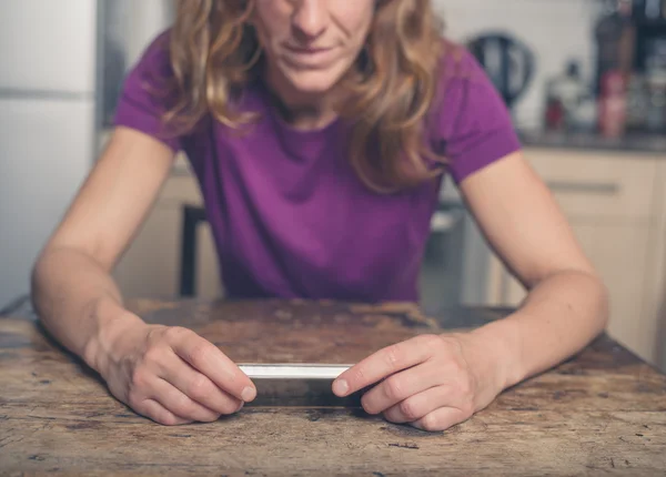 Mujer joven usando el teléfono inteligente en la cocina — Foto de Stock