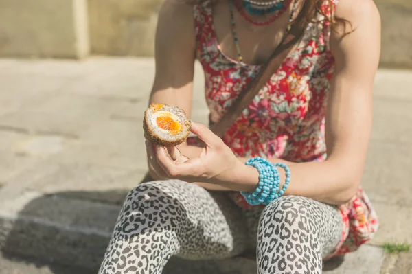 Mujer joven comiendo huevo escocés en la calle —  Fotos de Stock