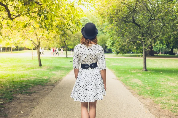 Kobieta nosi kapelusz i sukienka spaceru w parku — Zdjęcie stockowe