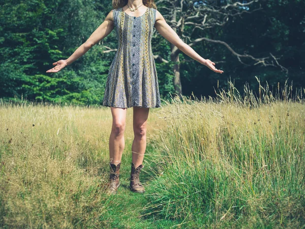 Junge Frau im Kleid hebt die Arme auf der Wiese — Stockfoto