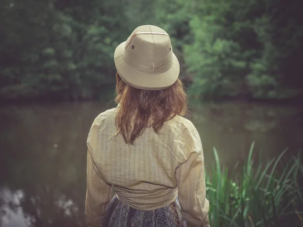 Mujer joven con sombrero de safari por estanque en el bosque —  Fotos de Stock