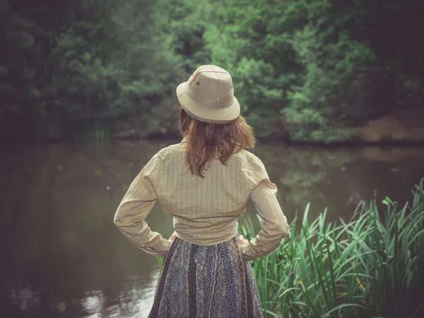 Mujer joven con sombrero de safari por estanque en el bosque —  Fotos de Stock