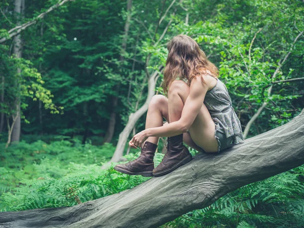 Young woman sitting on fallen tree in forest — Stock Photo, Image