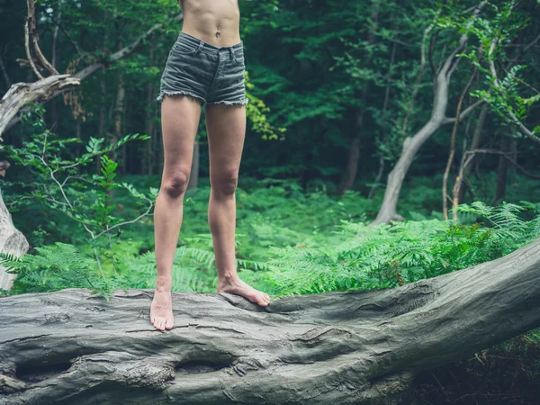 Joven mujer descalza de pie sobre un árbol caído en el bosque — Foto de Stock