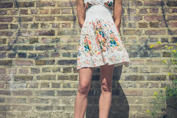 Young woman in dress standing by brick wall — Stock Photo, Image