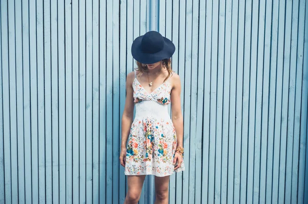 Woman in dress with hat outside by blue fence — Stock Photo, Image