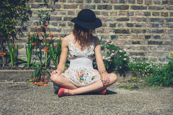 Giovane donna seduta vicino ai fiori fuori — Foto Stock
