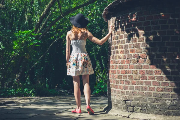 Mladá žena v šatech a klobouk cihlová zeď — Stock fotografie