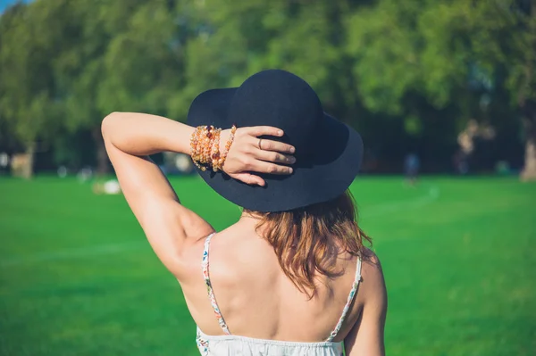 Young woman with hat standing in park — Stock Photo, Image