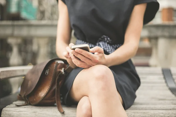 Молодая женщина на скамейке в городе с телефоном — стоковое фото