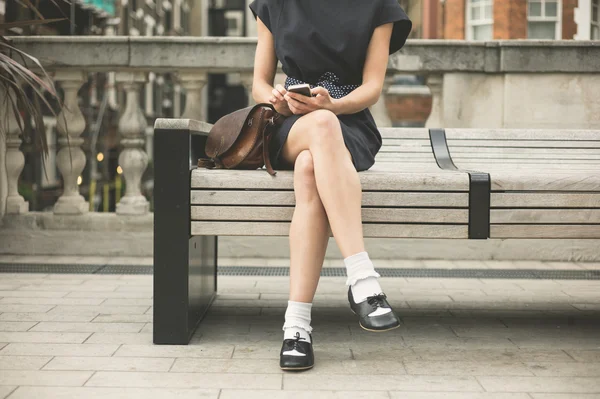 Giovane donna su panchina in città con telefono — Foto Stock