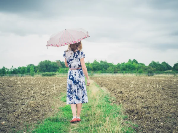 Mulher andando em campo estéril com guarda-chuva — Fotografia de Stock