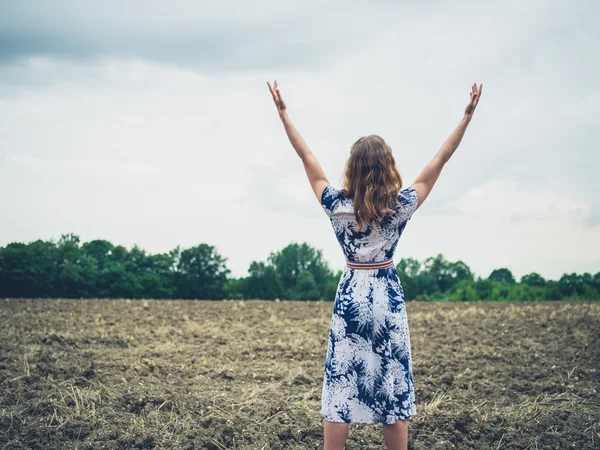 Woman raising her arms in barren field — Stock Photo, Image