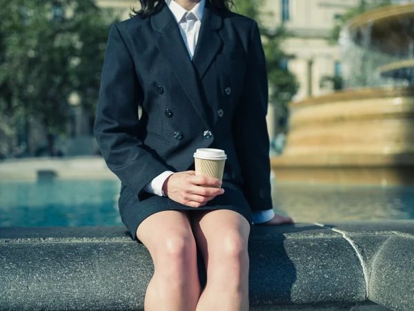 Young businesswoman with coffee by fountain — Stockfoto