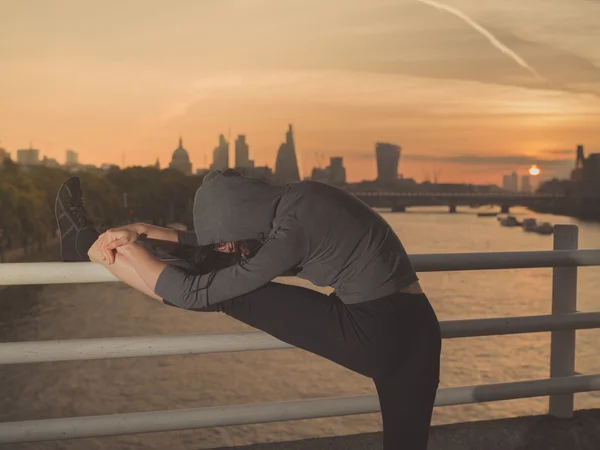 Fitness woman stretching leg on bridge at sunrise — Stok fotoğraf