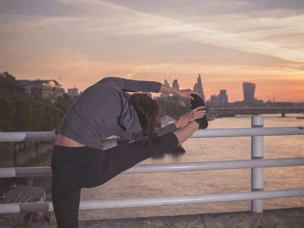 Fitness woman stretching leg on bridge at sunrise — Zdjęcie stockowe