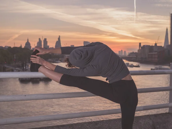 Fitness woman stretching leg on bridge at sunrise — 图库照片