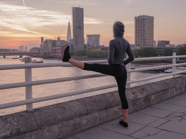 Fitness woman stretching leg on bridge at sunrise — Stock fotografie