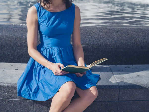 Young woman reading by fountain in the city — Stock Photo, Image