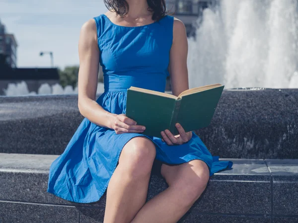 Jonge vrouw lezing van de fontein in de stad — Stockfoto