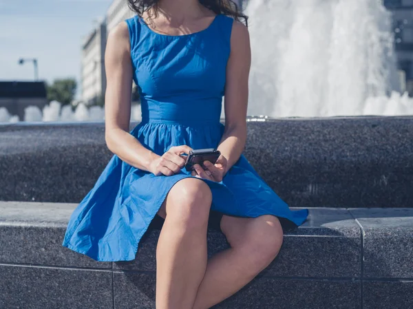 Young woman using smart phone by fountain in city — Stock Photo, Image