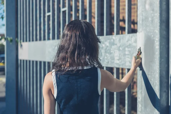Junge Frau greift nach Vorhängeschloss an Tor — Stockfoto