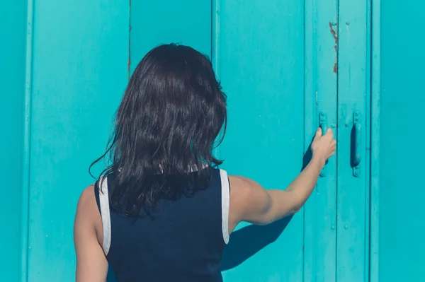 Jonge vrouw grijpen blauwe deur — Stockfoto