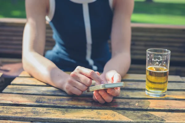 Mujer joven usando el teléfono inteligente y beber cerveza —  Fotos de Stock