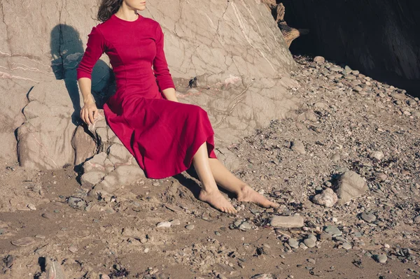 Mujer en vestido rojo relajante por cueva en la playa —  Fotos de Stock