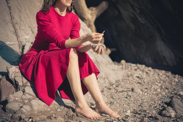 Mujer en vestido rojo relajante por cueva en la playa — Foto de Stock
