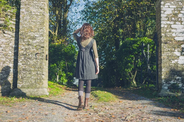 Young woman walking through stone gate — Stock Photo, Image