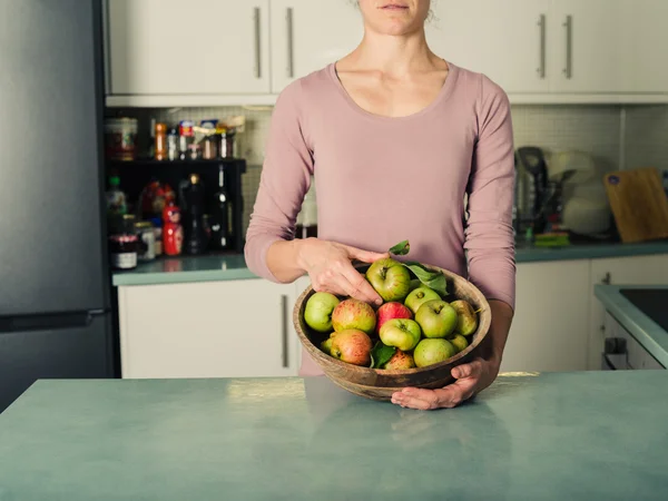 Ung kvinna i köket med skål med äpplen — Stockfoto