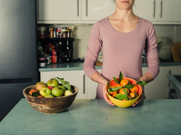 Ung kvinna med äpplen och apelsiner i kök — Stockfoto