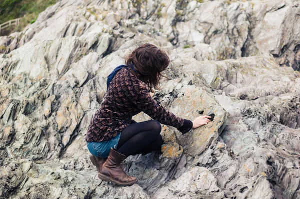 Jonge vrouw zitten op de rotsen en raken steen — Stockfoto